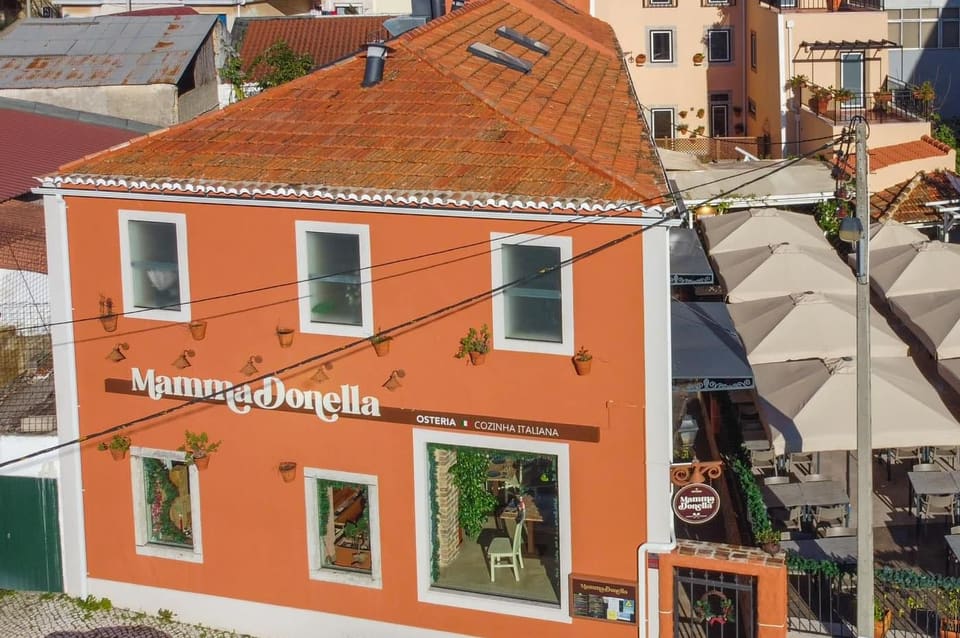 Fachada terracota de Massamá vista do alto, com o nome Mamma Donella na faixa castanha e a esplanada de chapéus de sol ao lado