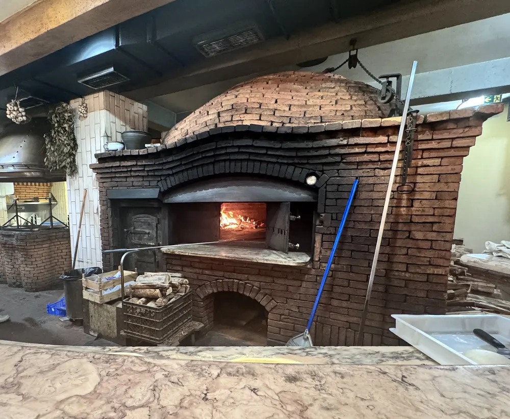 Forno a lenha de cúpula de tijolo aceso, com lenha empilhada por baixo
